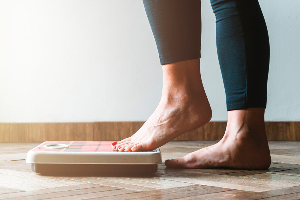 Woman shown from the calf down stepping on a scale to weigh herself 