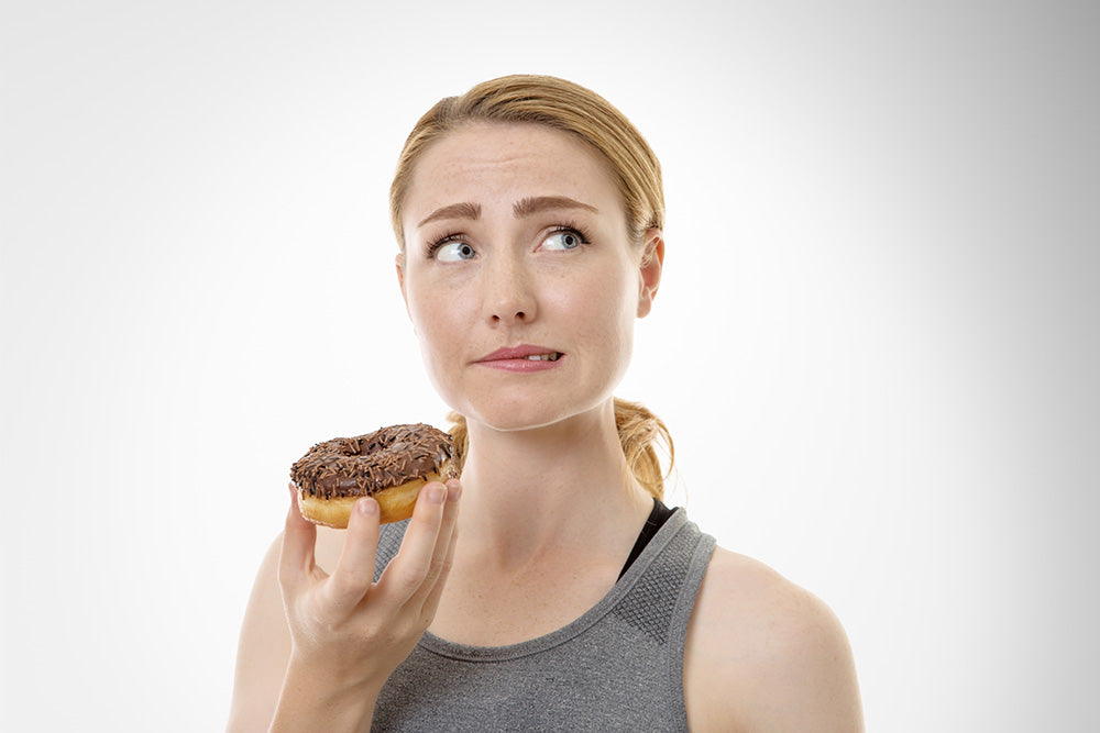 Woman looking tentative and guilty about eating a chocolate glazed donut
