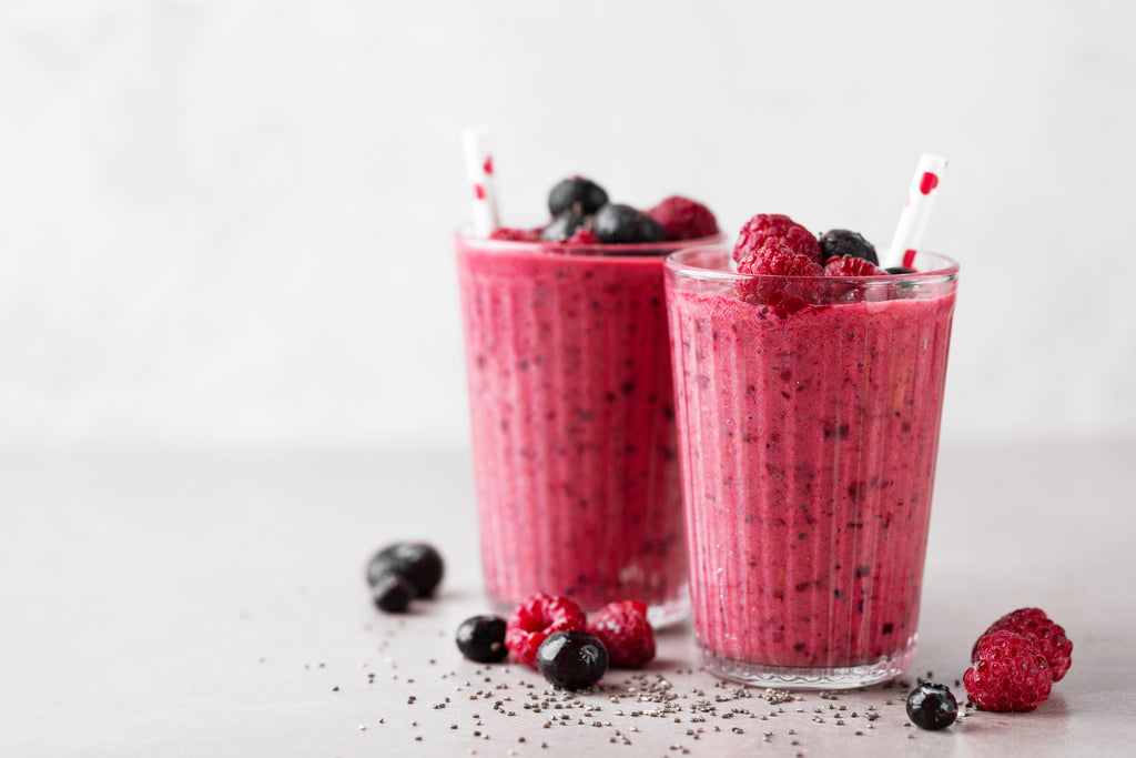 Fruit smoothies with straws and raspberries and blueberries around them