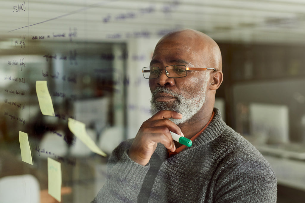 Older black man thinking and focusing on post it notes on a glass window