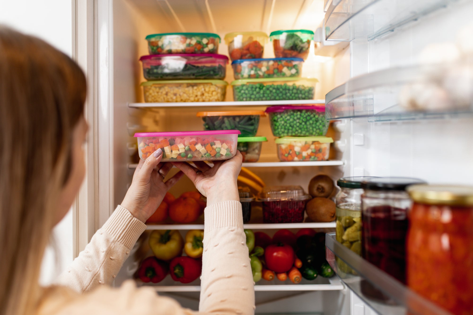 Woman putting Tupperware of fruits and vegetables in the fridge for meal prep