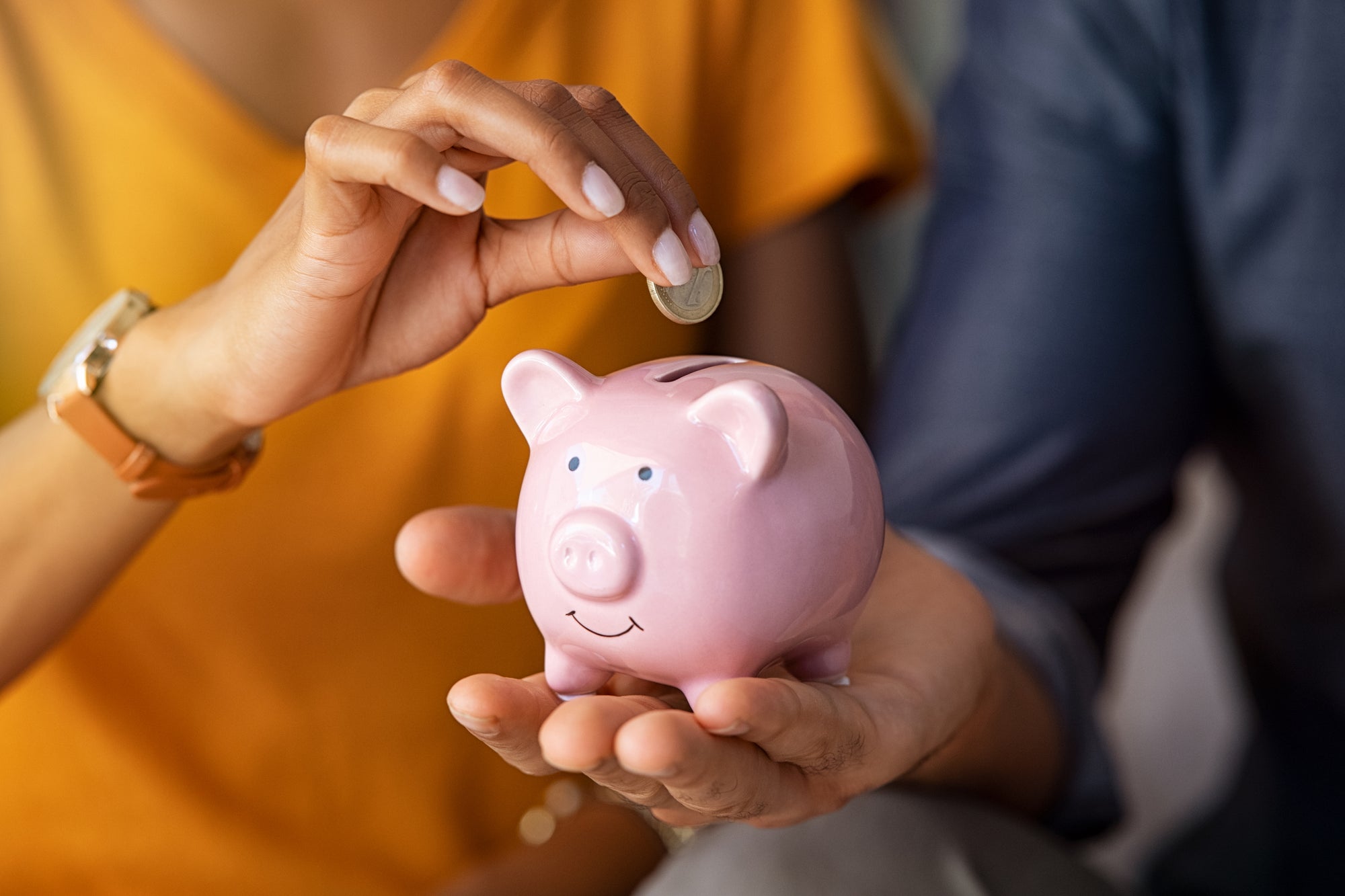 Man holding a piggy bank while woman puts coins in it