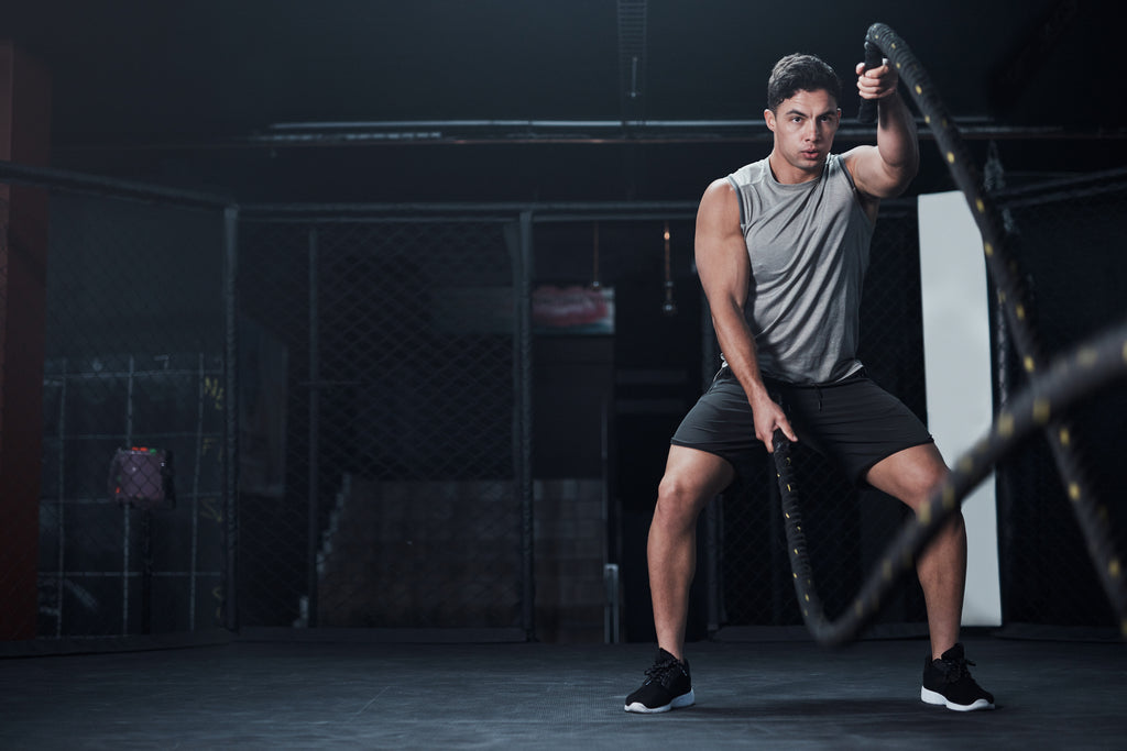 Man wearing gray tanktop and shorts doing battle rope exercises at the gym