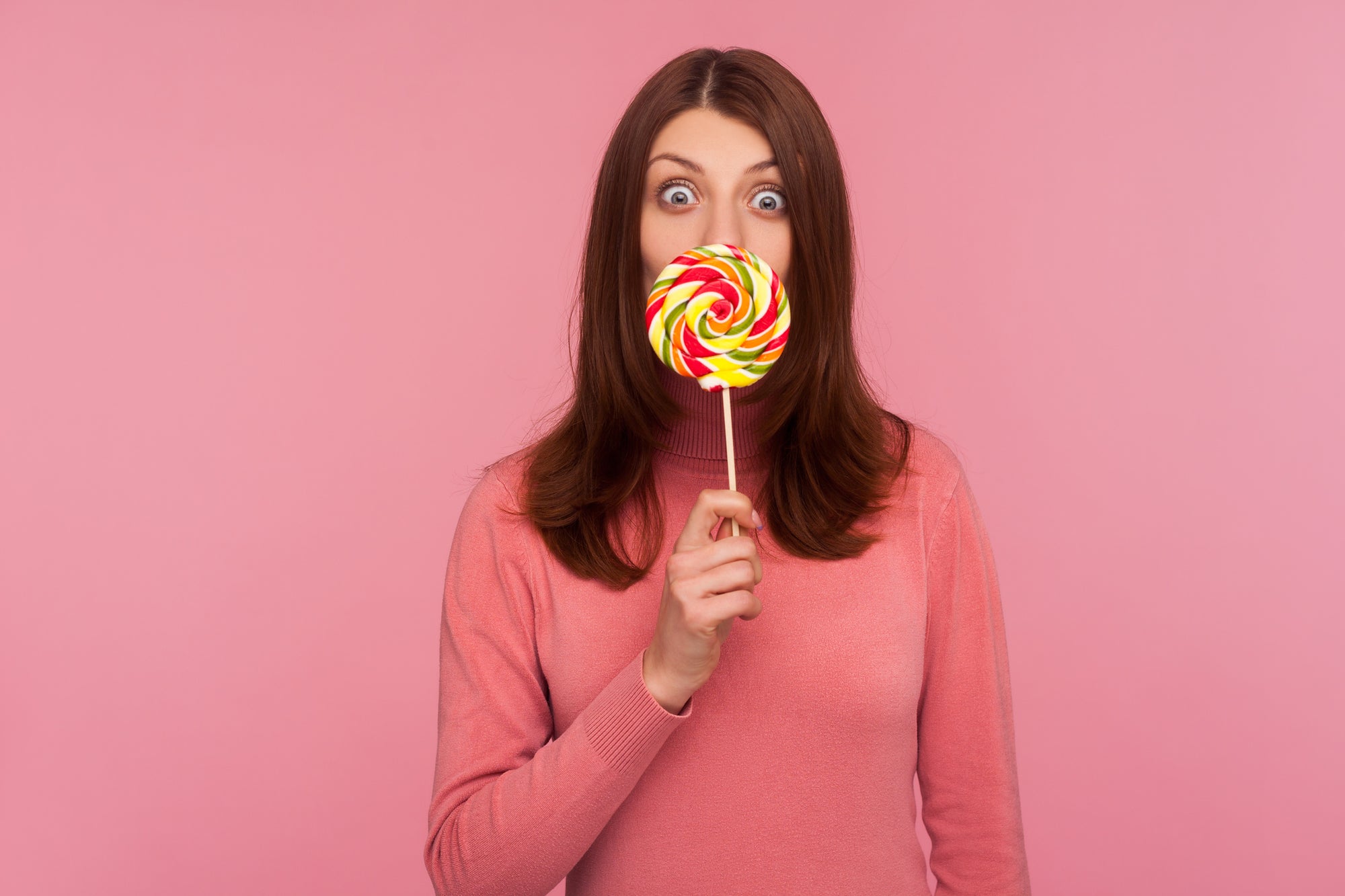 Woman in a pink sweater holding a rainbow lollipop