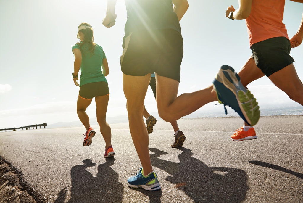 People's legs running outside on the pavement with the sun shining