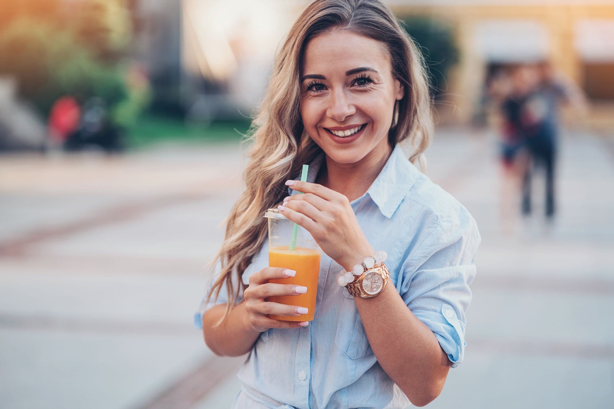 Blonde woman drinking an orange smoothie through a straw